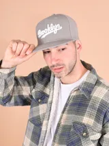 Gorro gris con visera plana y bordado frontal con la palabra "Brooklyn" en blanco.
