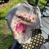 Buzo color crema de algodón con cuello redondo y mangas largas. Presenta un pequeño estampado de una lata de mermelada de frutilla en el pecho.