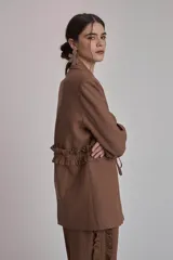 Blazer marrón con solapas de muesca, cierre frontal con lazo y mangas largas. Presenta volados a lo largo de las costuras laterales del pantalón a juego.