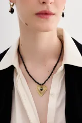 Collar de cadena de cuentas irregulares negras con dije central de corazón texturizado dorado y detalle de piedra negra.