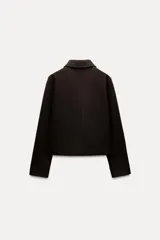 Chaqueta corta negra de cuello solapa y manga larga con puños. Tiene bolsillos de parche en el frente y cierre frontal con botones.