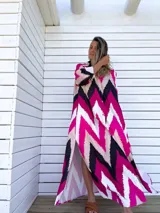 Vestido camisero largo con estampado chevron en fucsia, beige y negro, con cuello camisero, mangas largas y abotonadura frontal. Presenta aberturas laterales en el ruedo.