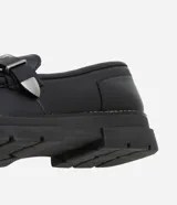 Zapato negro de cuero sintético con punta redonda, detalle de hebilla plateada y suela track.