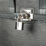 Cartera negra de cuero con relieve, diseño clásico y atemporal, con asas fijas y correa regulable. Tiene cierre superior, un compartimento y logotipo metálico.
