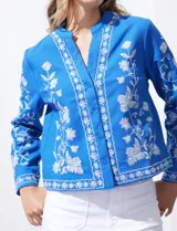 Chaqueta de algodón bordada, color azul con bordado floral blanco, con cuello a la base y escote en V, abertura central con botón.