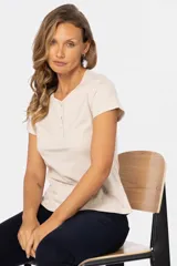 Remera color beige de corte clásico, con cuello redondo y mangas cortas. Presenta una botonadura frontal parcial con botones personalizados.