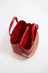 Bolso tote negro de cuero vacuno con doble asa corta y correa de tela extraíble. Interior con tres compartimentos y bolsillo con cremallera. Logo metálico de la marca en el frente.