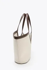 Bolso tipo shopper color crudo, con cuerpo de lona y detalles en cuero marrón. Tiene doble asa de hombro y una bolsa interior extraíble con cierre de cremallera. Se cierra con un lazo.