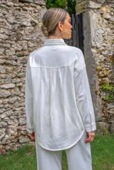 Camisa blanca de algodón con cuello clásico, cierre frontal con botones metálicos a presión, dos bolsillos de parche en el pecho y apliques de brillos en la parte delantera.