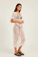 Kimono largo de encaje blanco con diseño holgado, cuello profundo y ajuste mediante cordón fino en la cintura. Presenta un patrón floral calado y mangas cortas amplias, ideal para usar como salida de baño.