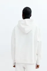 Canguro holgado color blanco, con capucha forrada con cordón ajustable, bolsillo tipo canguro, puños y bajo en punto elástico.