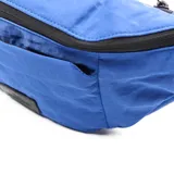 Riñonera azul de tela con correa ajustable negra, cierre superior y bolsillo frontal.