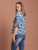 Blusa blanca de gasa marca Sioni, con cuello a la base y escote en V. Tiene abertura central con botones y mangas 3/4 con terminación fruncida.