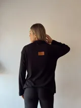 Sweater negro de punto canalé con cuello polo y etiqueta de cuero sintético en la espalda.