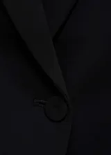 Blazer negro de corte entallado con solapas de muesca, cierre cruzado con un botón, bolsillos delanteros con solapa y manga larga con puños abotonados.