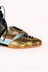 Zapato tipo blucher botín de seda salvaje color dorado con rejilla blocada en la talonera y ribetes de terciopelo negro. Tiene cordones negros y plantilla intercambiable con cuña interna de 1,5cm. Modelo exclusivo diseñado y fabricado en España.