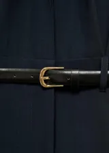 Mono largo negro de corte slim, con cuello camisero, cierre frontal abotonado, cinturón con hebilla dorada, dos bolsillos de parche con solapa en el pecho y puños abotonados.