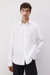 Camisa blanca de lino con cuello inglés, tapeta clásica y canesú en la espalda. Mangas largas con tapeta de manga y botón, y cierre ajustable de botón en los puños. Bajo redondeado. Corte estándar.