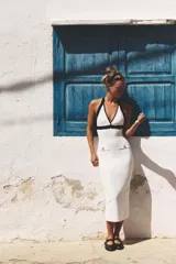 Vestido midi blanco de tejido elástico, con cuello halter, escote pico, falsos bolsillos de vivo con botón y acabados a contraste en negro.