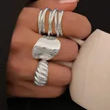 Set de tres anillos plateados con diferentes diseños: uno con forma irregular, otro con diseño de espiral y otro con múltiples líneas paralelas.