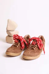 Zapatillas bajas marrones de gamuza con cordones y detalle de aplique de fresa en los cordones.