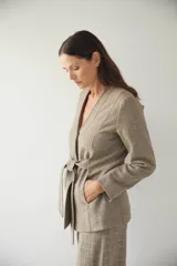 Chaqueta corta color beige, entallada, con escote en V, manga larga y cierre frontal con lazo fijo. Confeccionada en lana fina sin teñir, con bolsillos escondidos y terminaciones enviadas. Hecha 100% en Uruguay.