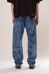Pantalón de denim azul con diseño abstracto en tono más claro, de corte wide leg y cinco bolsillos.