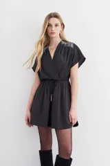 Minivestido negro de escote cruzado, mangas cortas y cintura elastizada con lazo. Presenta cadenitas metálicas en los hombros y en los extremos del lazo.