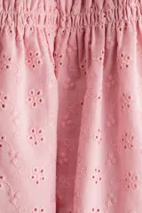 Vestido corto rosado en tejido de algodón con broderie, escote recto, breteles anchos fruncidos, cuerpo entallado con frunces elásticos y pollera con leve vuelo. Ribete de volados en escote y breteles. Forrado.