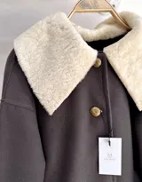 Sobre camisa marrón oscuro de paño de lana con cuello y puños de cuero de cordero color crema. Cierre frontal con botones dorados con el escudo de Uruguay.