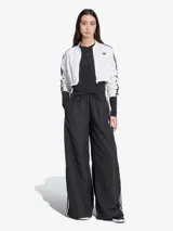 Pantalón deportivo negro de corte ancho con tres rayas blancas verticales en los laterales y logo de Adidas bordado en blanco en la parte superior de la pierna izquierda.