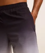 Bermuda deportiva masculina con cintura elástica, cordón interno de ajuste y forro de malla. Diseño con cuadros difuminados en degrade de gris oscuro a blanco.