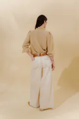 Blusa color beige con cuello mao con volantes, manga larga con puño elástico y cierre frontal con botones ocultos.