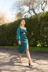 Vestido midi con estampado floral en tonos lila, amarillo y verde. Tiene escote fruncido con lazo ajustable, mangas largas abullonadas y tajo lateral.