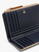 Billetera plegable color beige con estampado del logo de Tommy Hilfiger en toda la superficie. Tiene cierre de cremallera, múltiples ranuras para tarjetas, compartimento para billetes y bolsillo exterior para monedas.