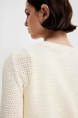 Cárdigan corto de punto texturizado color crema, con cuello redondo, cierre frontal con botones dorados y bolsillos frontales decorativos con botón dorado. Tiene terminaciones acanaladas en cuello, puños y ruedo.