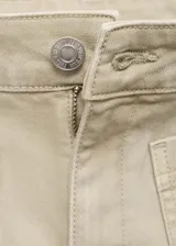 Pantalón de jean color beige, tiro medio, corte flare, con bolsillos de parche delanteros y ruedo desflecado.