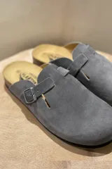 Zuecos grises marca Plakton, confeccionados en cuero vacuno, con hebilla lateral ajustable, plantilla anatómica con memory cushion y suela de goma y corcho.