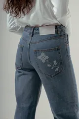 Pantalón de denim azul claro, tiro alto, de corte recto y pierna ancha. Presenta detalles bordados en el área de los bolsillos delanteros y traseros.