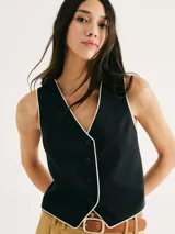 Chaleco blanco con ribete negro, cuello en V y cierre frontal con botones.