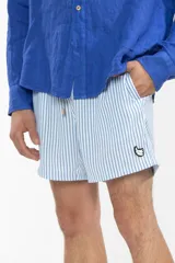 Short de baño celeste con rayas verticales blancas, cintura elástica con cordón ajustable, bolsillos laterales y trasero con cierre, logo de la marca bordado en la pierna.