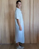 Vestido camisero de denim azul con cuello clásico, cierre frontal con botones y mangas cortas con dobladillo.