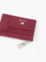 Tarjetero de cuero vacuno color bordó con aplique metálico de flor y tiracierre con diseño exclusivo.