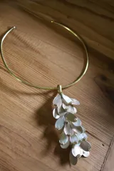 Gargantilla rígida dorada con dije colgante de pétalos dorados y blancos con incrustaciones de strass.