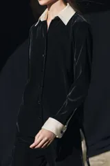 Camisa negra de terciopelo con cuello solapa, manga larga con puños en tejido color crema a contraste y bajo redondeado.