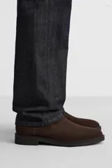 Bota Chelsea de cuero marrón oscuro con elásticos laterales negros, tirador trasero y suela plana.