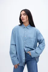 Camisa celeste de denim de algodón, con cuello solapa clásico, bolsillo cuadrado en el pecho, botones personalizados y calce oversize.