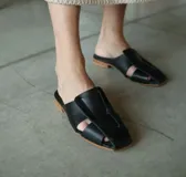 Zueco de cuero negro abierto en la parte delantera, con suela de madera, diseño elegante y cómodo.