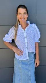 Camisa blanca con estampado floral, cuello mao con volados y mangas cortas abullonadas con puños elásticos.