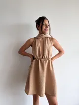 Vestido corto color beige, con escote halter y espalda descubierta. Presenta cintura elastizada y falda con vuelo.